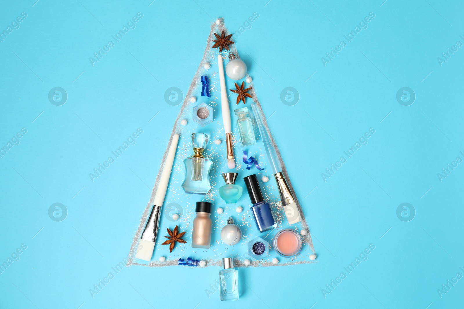 Photo of Christmas tree made of perfume bottles and makeup products on light blue background, flat lay