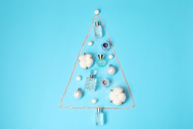 Photo of Christmas tree made of perfume bottles and cotton flowers on light blue background, flat lay