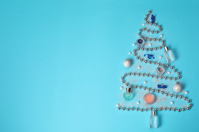 Photo of Christmas tree made of perfume bottles and makeup products on light blue background, flat lay. Space for text