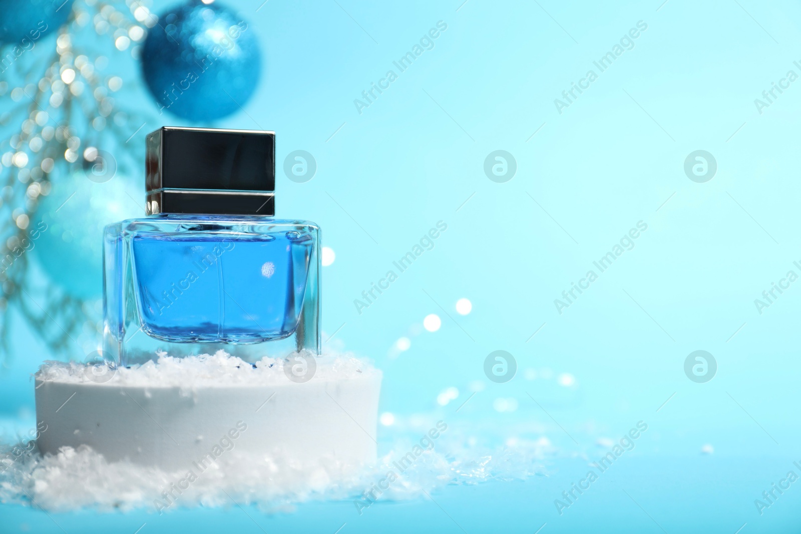 Photo of Christmas composition with perfume bottle and snow on light blue background, closeup. Space for text