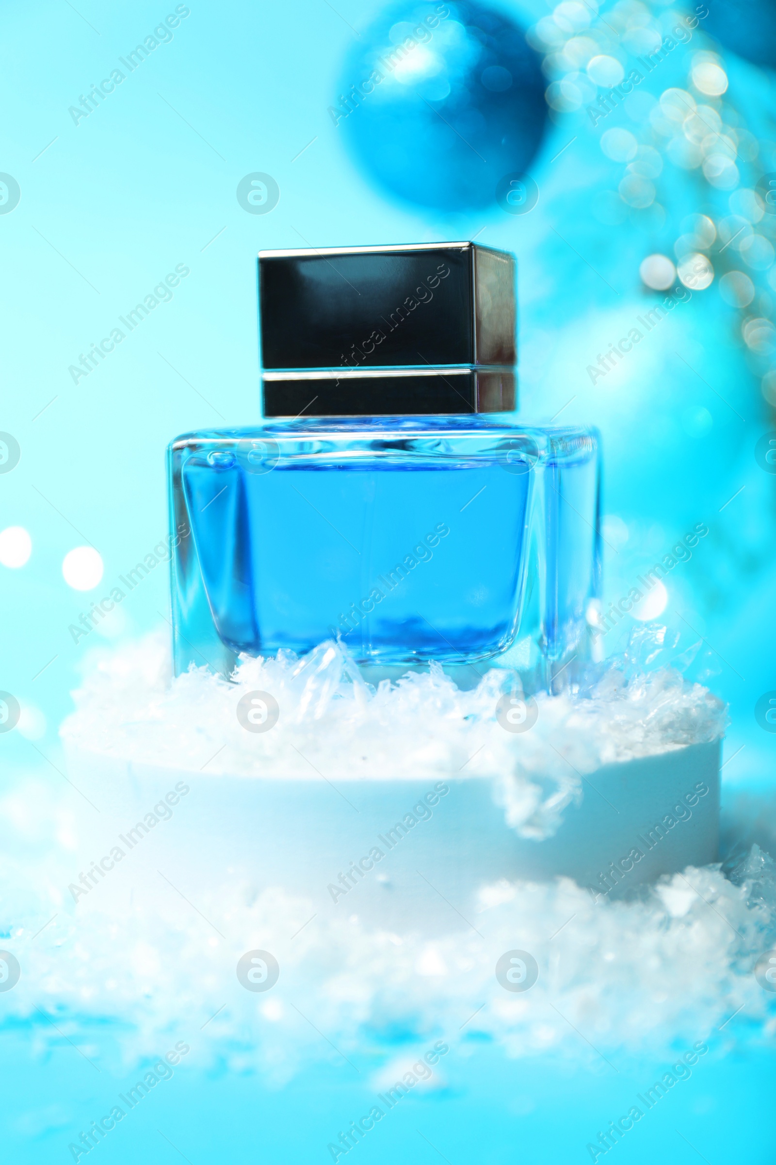 Photo of Christmas composition with perfume bottle and snow on light blue background, closeup