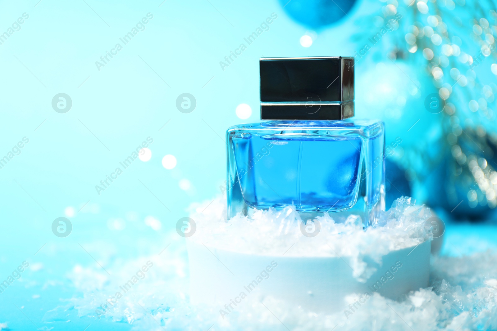 Photo of Christmas composition with perfume bottle and snow on light blue background, closeup. Space for text