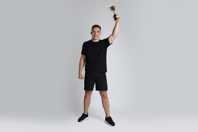 Happy winner with golden trophy cup on light grey background