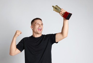 Happy winner with golden trophy cup on light grey background