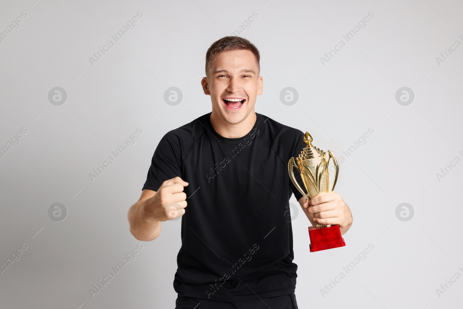 Photo of Happy winner with golden trophy cup on light grey background