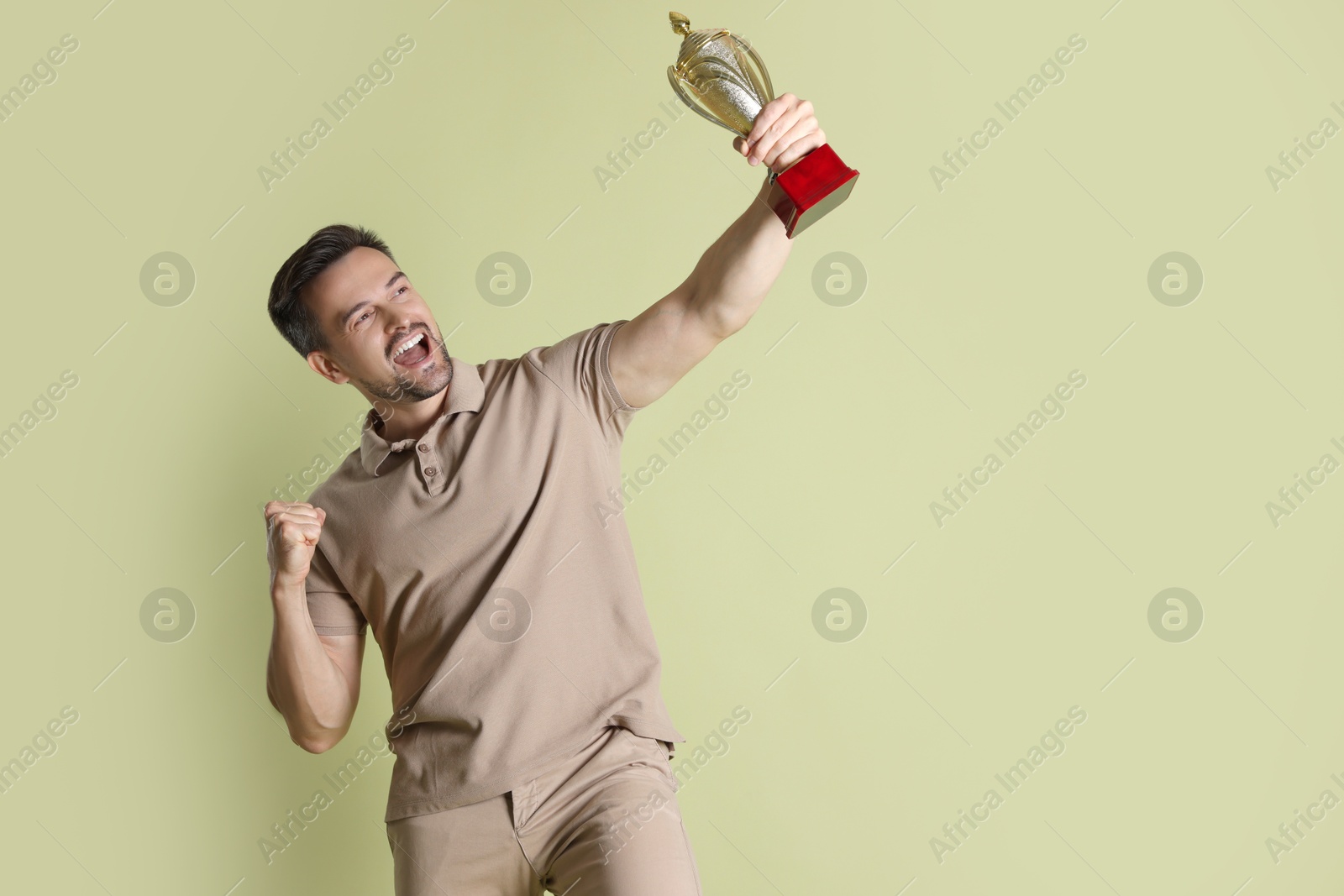 Photo of Happy winner with golden trophy cup on pale olive background, space for text