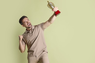 Photo of Happy winner with golden trophy cup on pale olive background, space for text