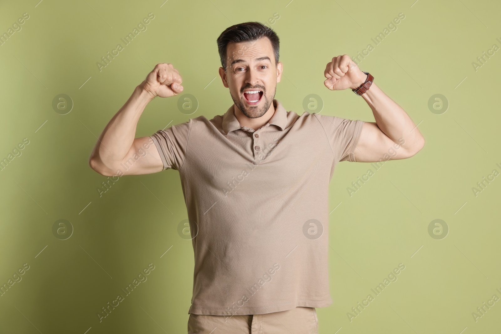 Photo of Happy winner showing his biceps on pale olive background