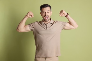 Happy winner showing his biceps on pale olive background