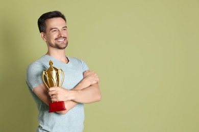 Photo of Happy winner with golden trophy cup on pale olive background, space for text