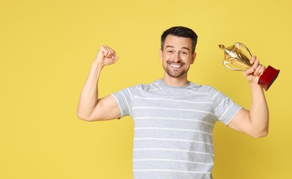 Photo of Happy winner with golden trophy cup showing his biceps on yellow background