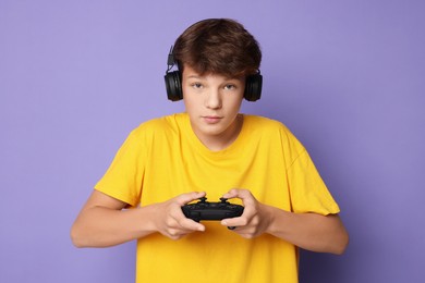 Photo of Teenage boy in headphones playing video game with controller on violet background