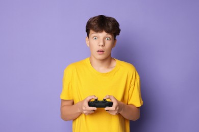 Emotional teenage boy playing video game with controller on violet background