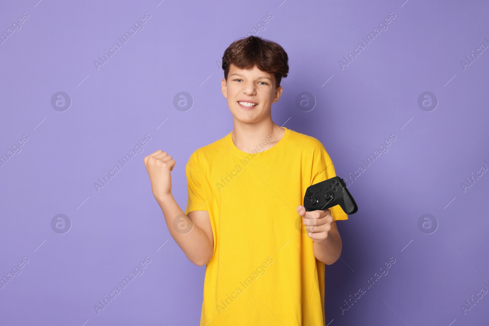 Photo of Happy teenage boy with controller on violet background