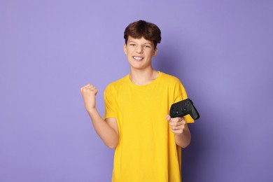 Photo of Happy teenage boy with controller on violet background