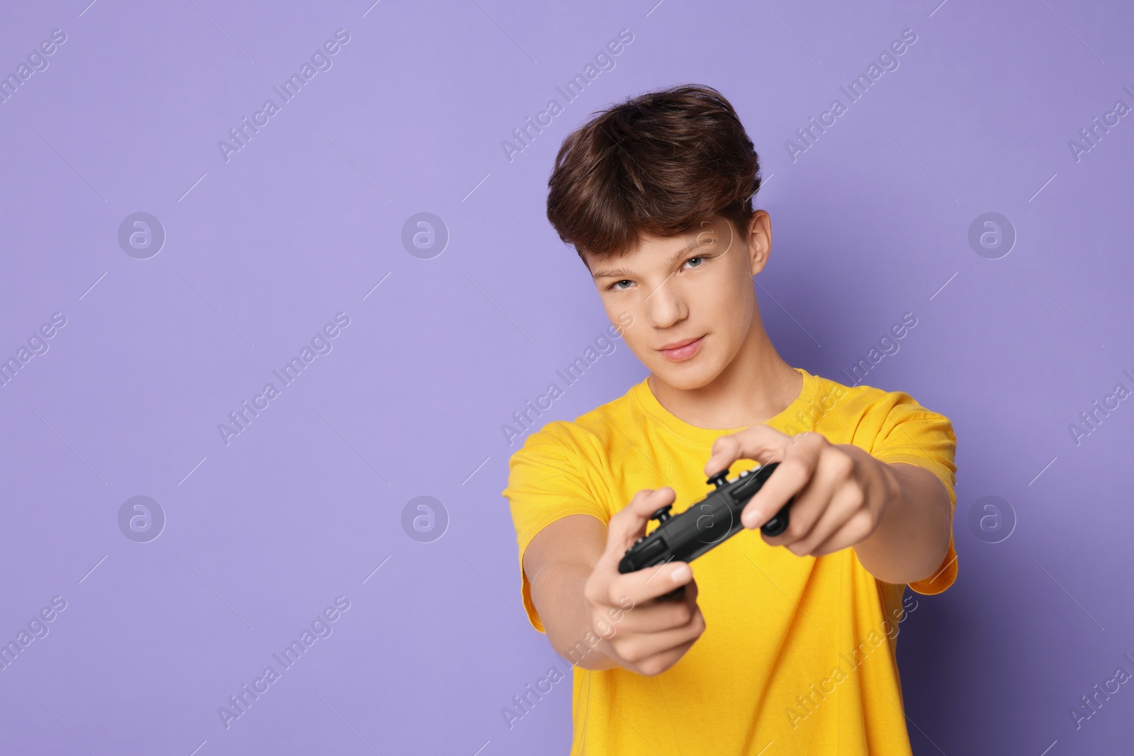 Photo of Teenage boy playing video game with controller on violet background. Space for text