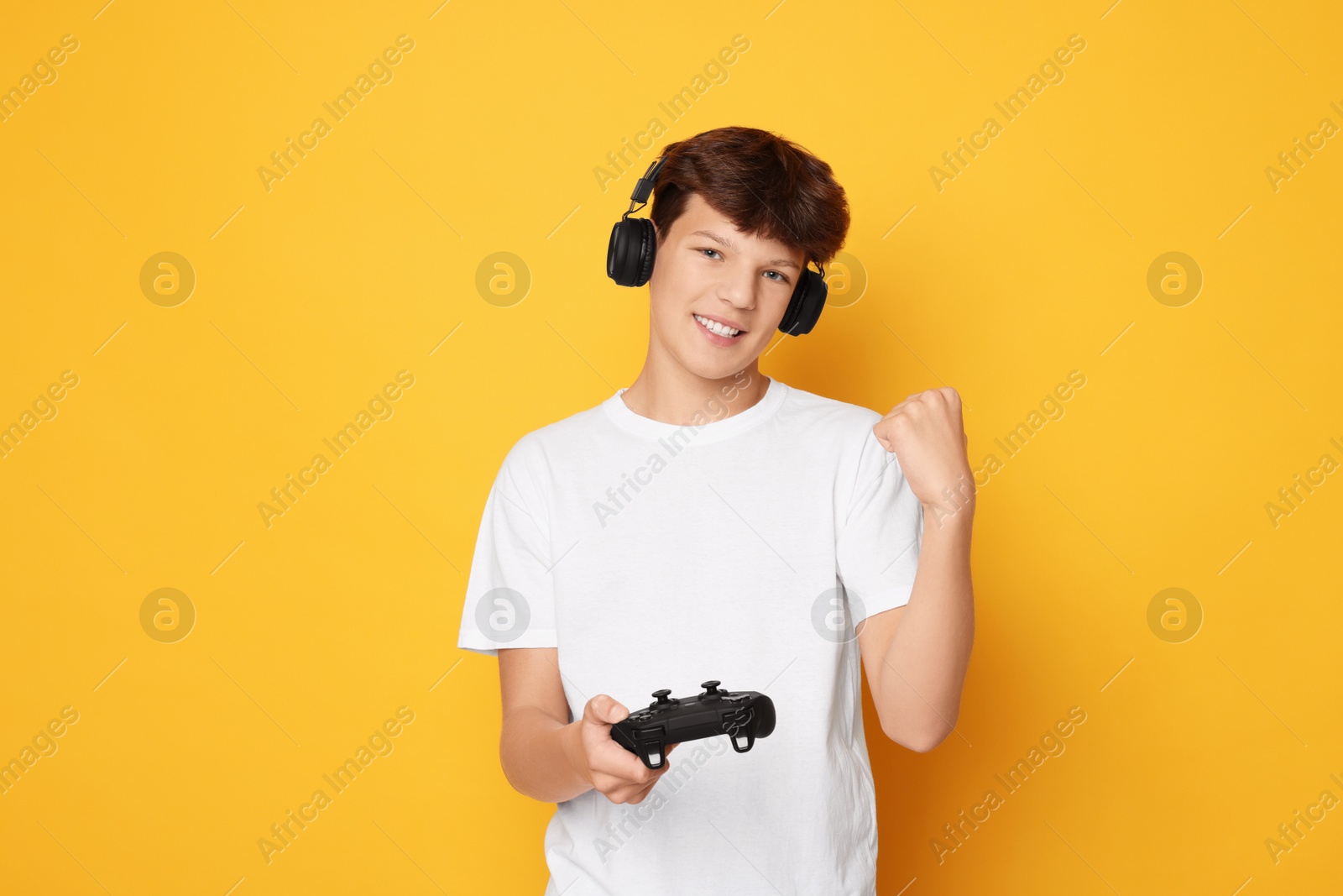 Photo of Happy teenage boy in headphones with controller on orange background