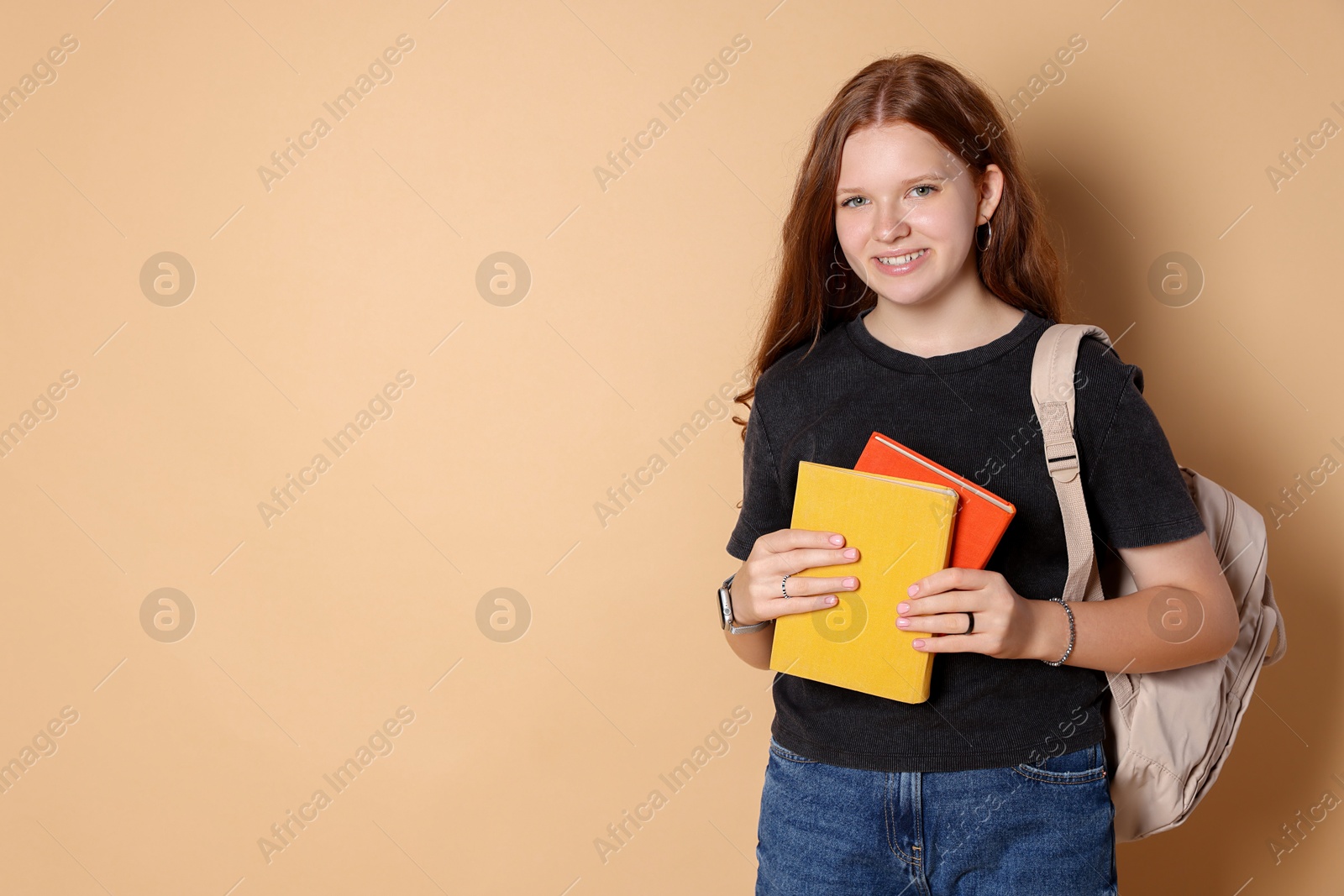 Photo of Smiling teenage girl with backpack and books on beige background. Space for text