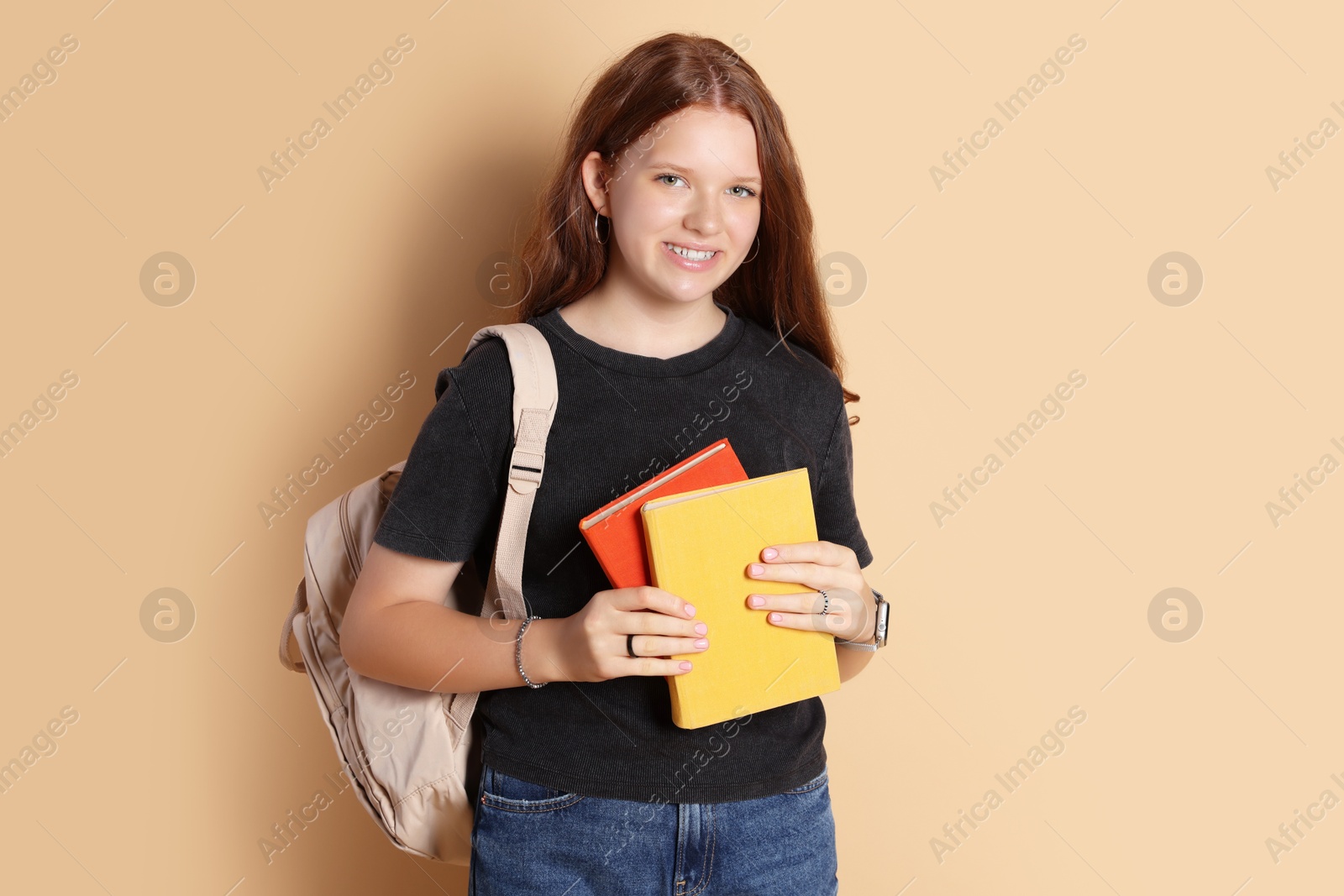 Photo of Smiling teenage girl with backpack and books on beige background