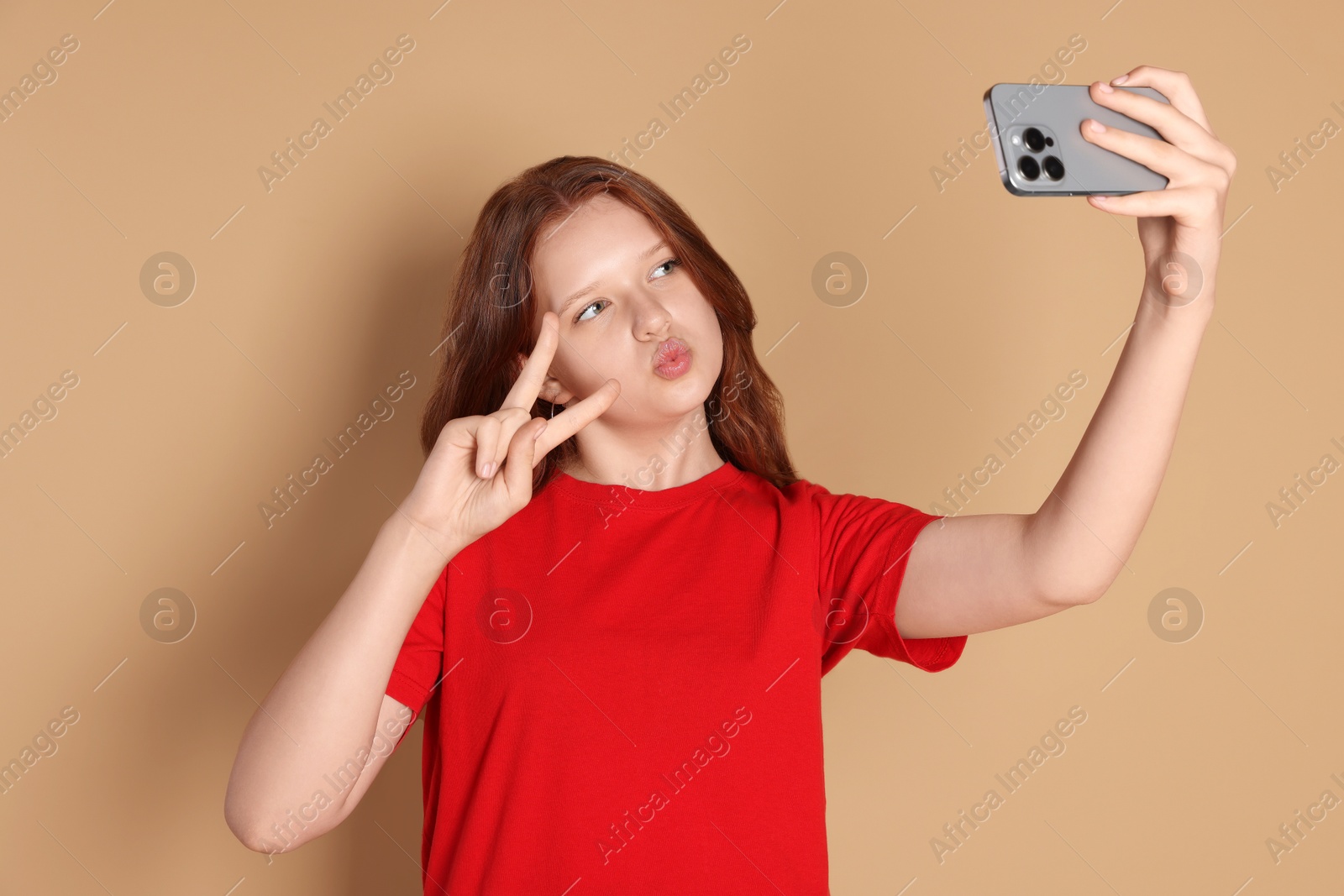 Photo of Cute teenage girl taking selfie and showing peace sign on beige background