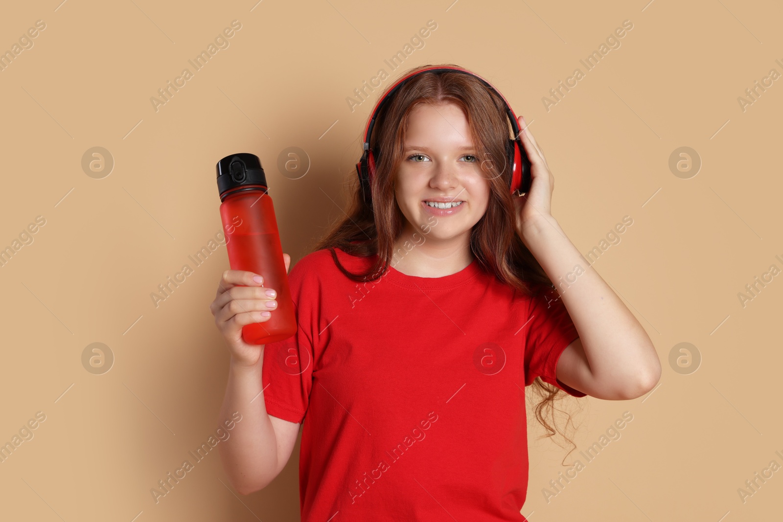 Photo of Smiling teenage girl with bottle listening to music on beige background