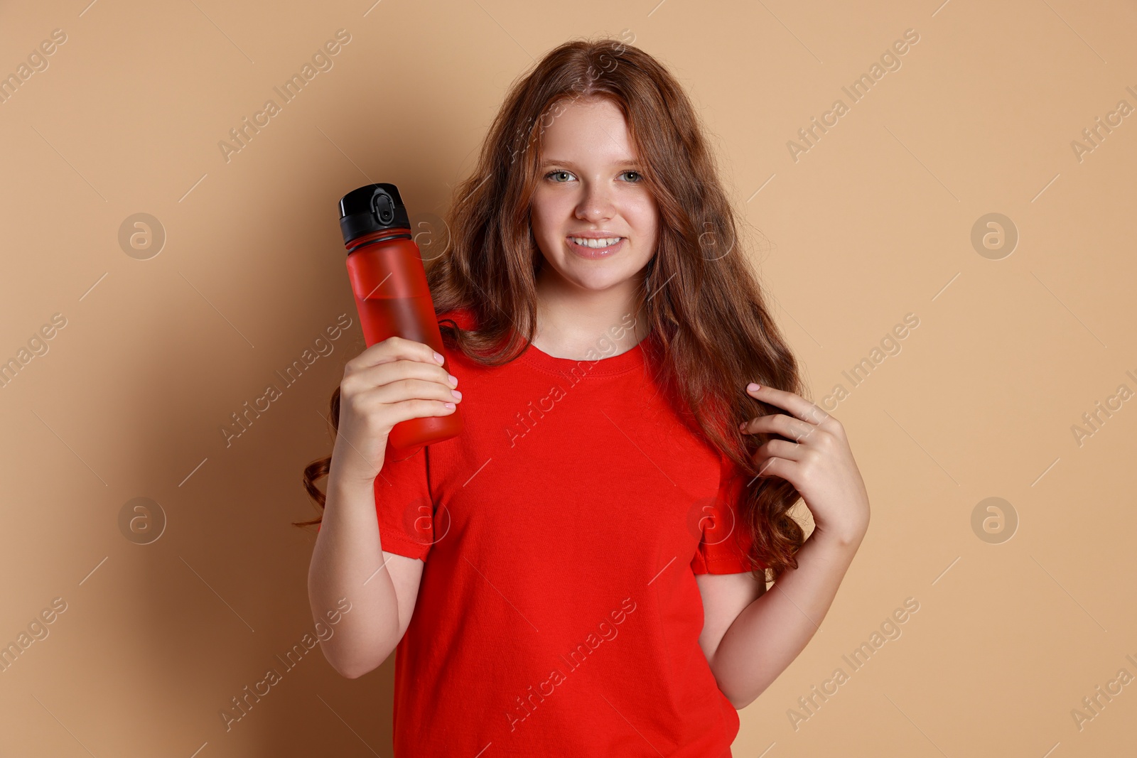 Photo of Smiling teenage girl with bottle on beige background