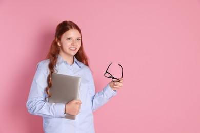 Smiling teenage girl with laptop and glasses on pink background. Space for text