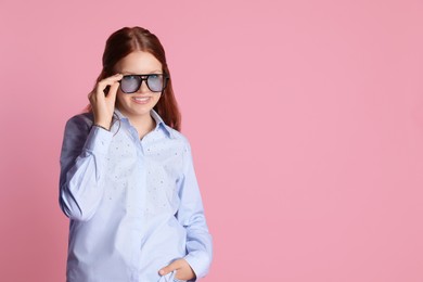 Happy teenage girl in sunglasses posing on pink background. Space for text