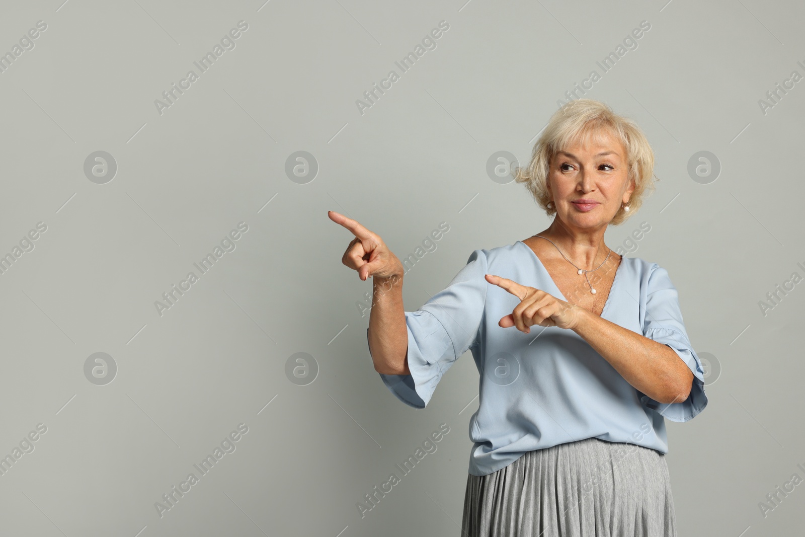 Photo of Beautiful senior woman pointing on light grey background, space for text