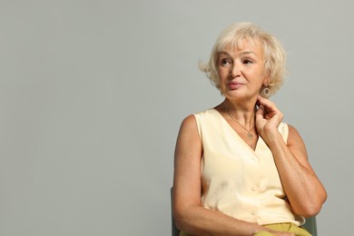 Beautiful senior woman sitting on chair against light grey background, space for text