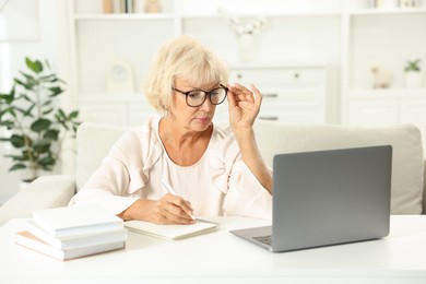 Beautiful senior woman using laptop at white table indoors