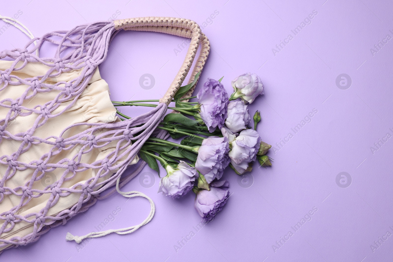 Photo of Handmade macrame shopping bag with flowers on violet background, top view