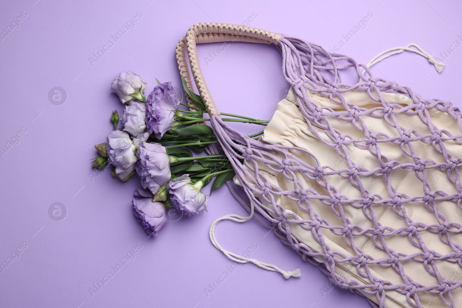 Photo of Handmade macrame shopping bag with flowers on violet background, top view