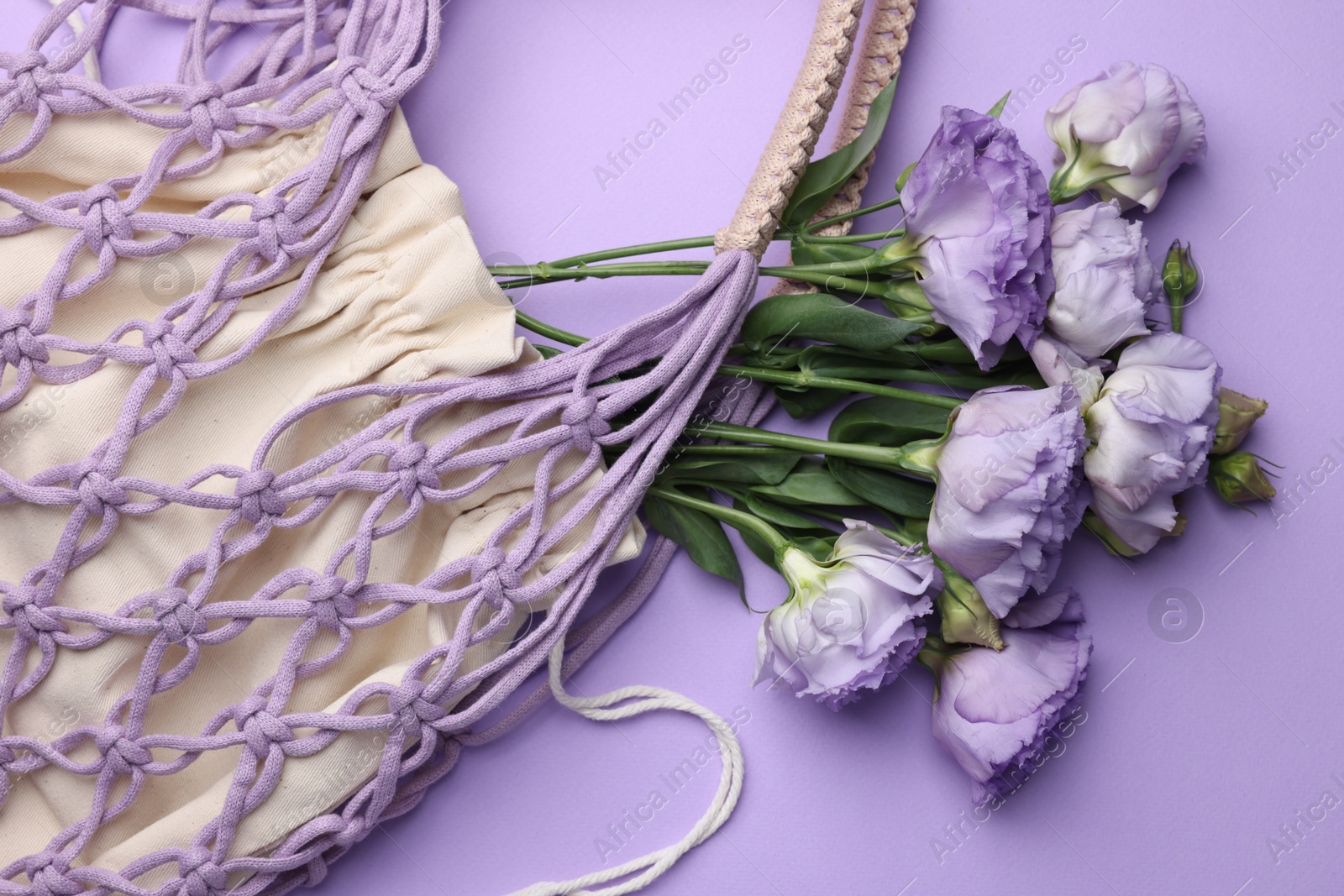 Photo of Handmade macrame shopping bag with flowers on violet background, top view