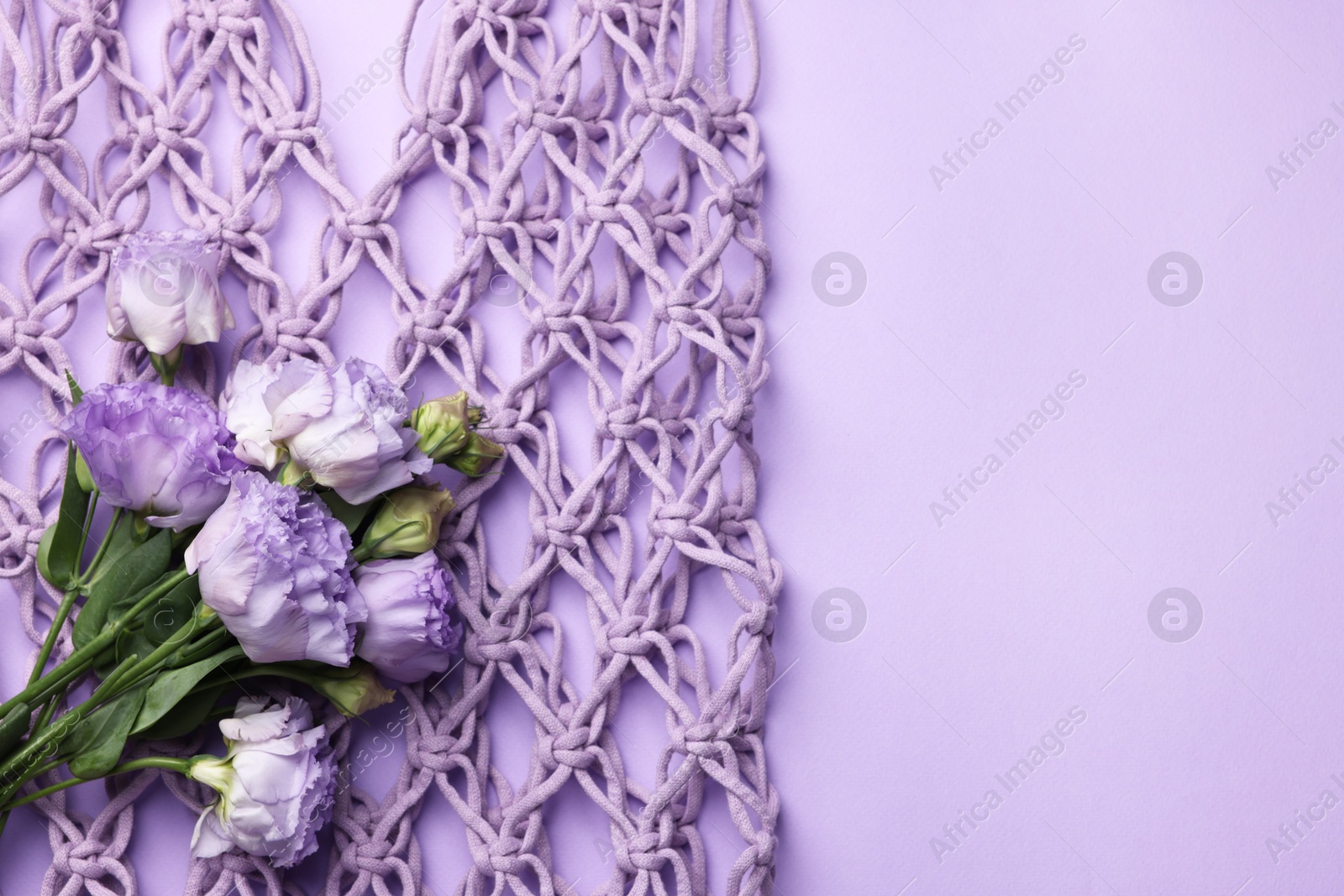 Photo of Handmade macrame shopping bag with flowers on violet background, top view. Space for text