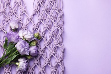 Photo of Handmade macrame shopping bag with flowers on violet background, top view. Space for text