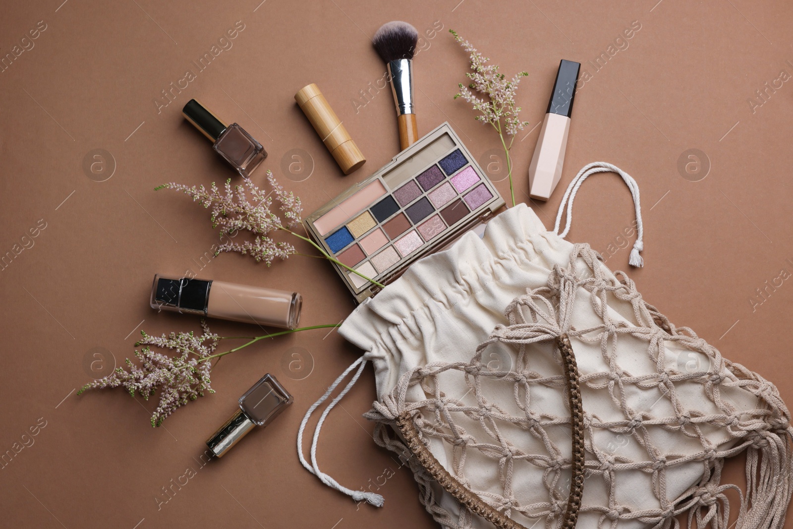 Photo of Handmade macrame shopping bag with makeup products and spikes on brown background, flat lay