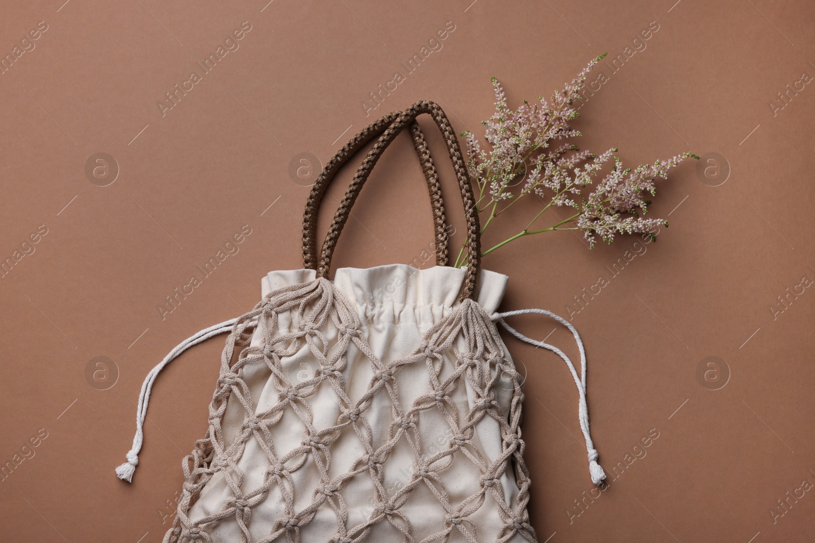 Photo of Handmade macrame shopping bag with spikes on brown background, top view