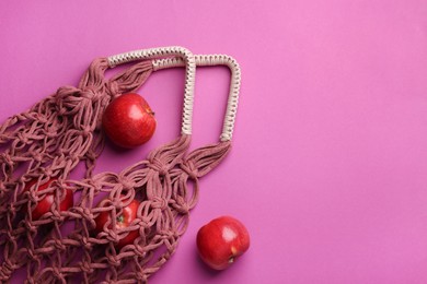 Photo of Handmade macrame shopping bag with apples on crimson background, top view. Space for text