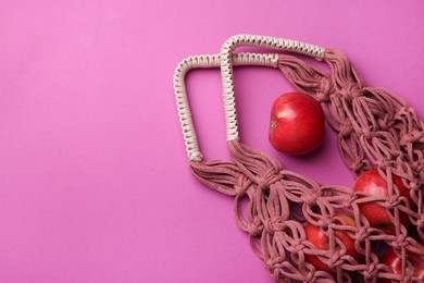 Photo of Handmade macrame shopping bag with apples on crimson background, top view. Space for text