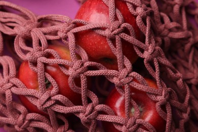 Photo of Handmade macrame shopping bag with apples on crimson background, closeup