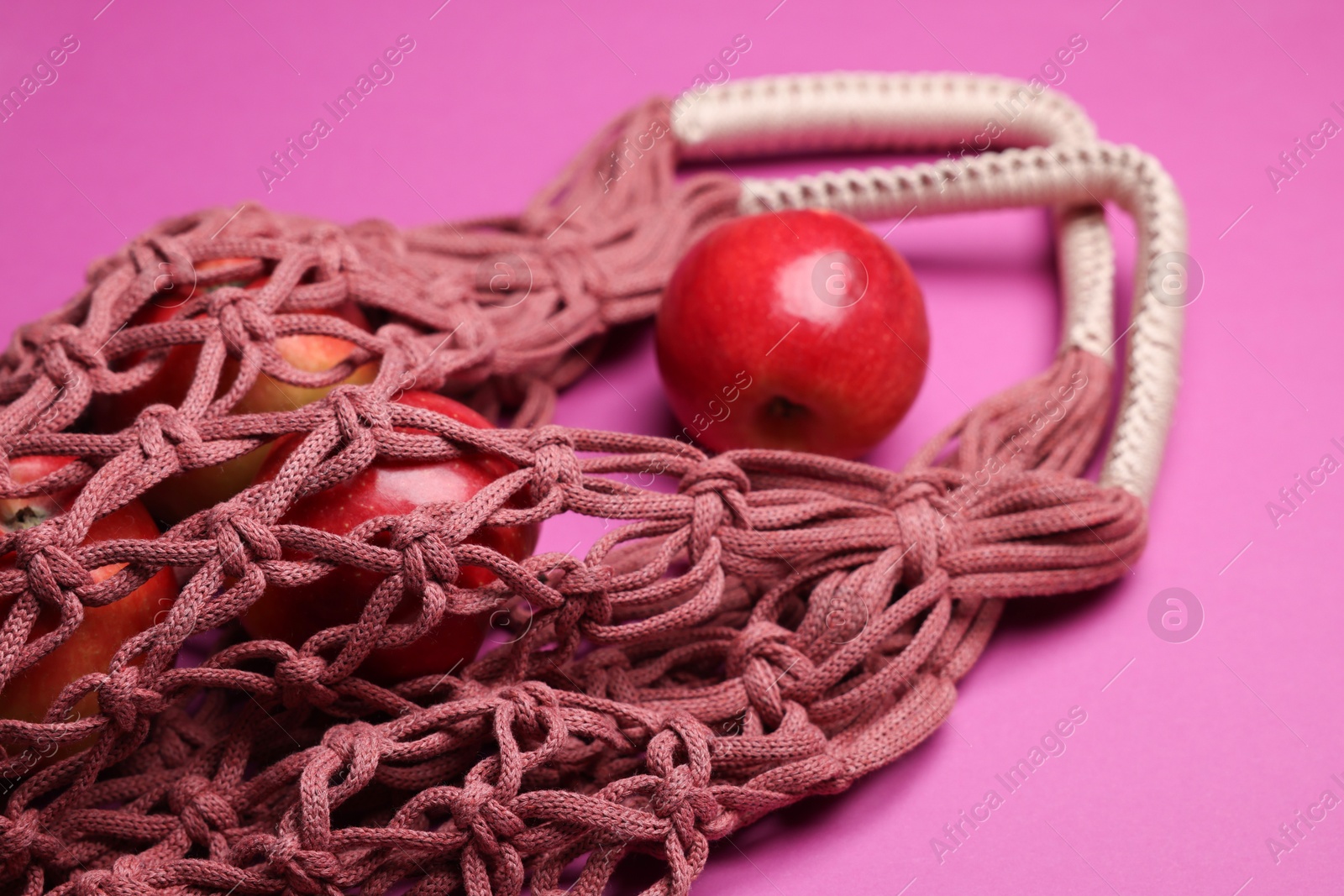 Photo of Handmade macrame shopping bag with apples on crimson background, closeup