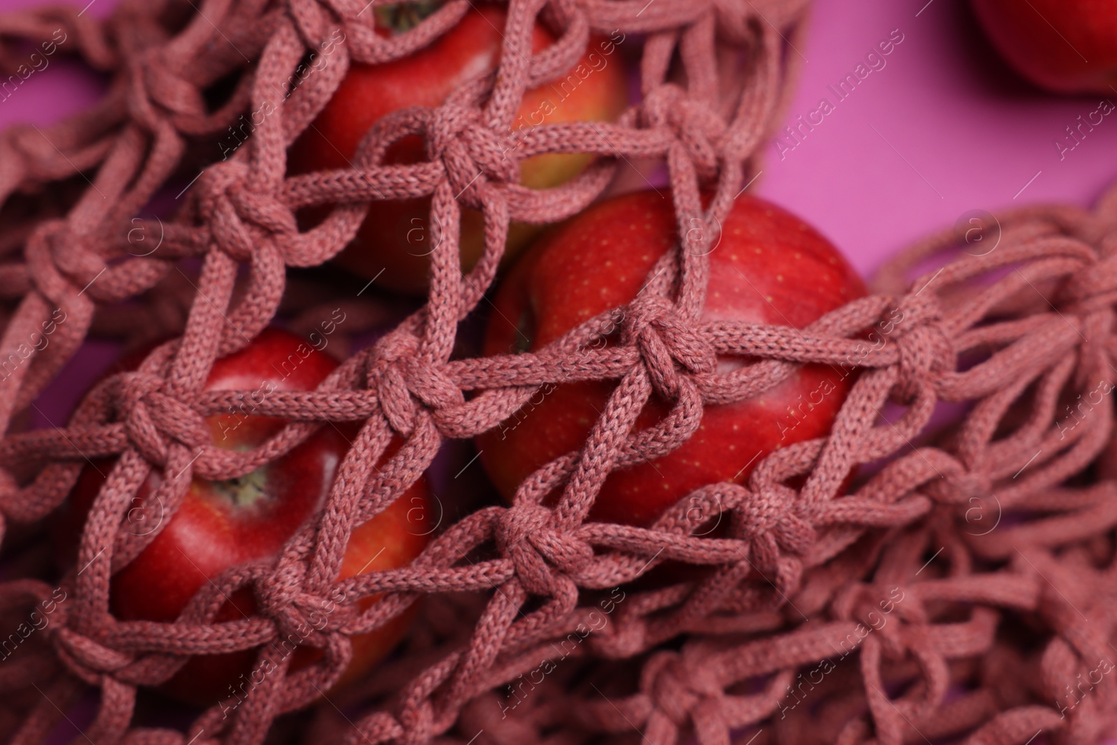 Photo of Handmade macrame shopping bag with apples on crimson background, closeup