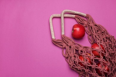 Photo of Handmade macrame shopping bag with apples on crimson background, top view. Space for text