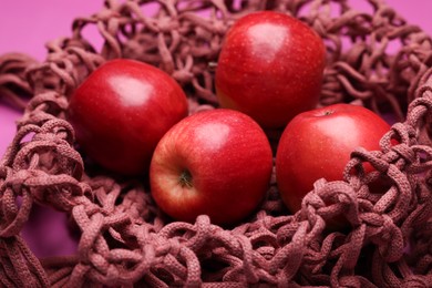 Photo of Handmade macrame shopping bag with apples on crimson background, closeup