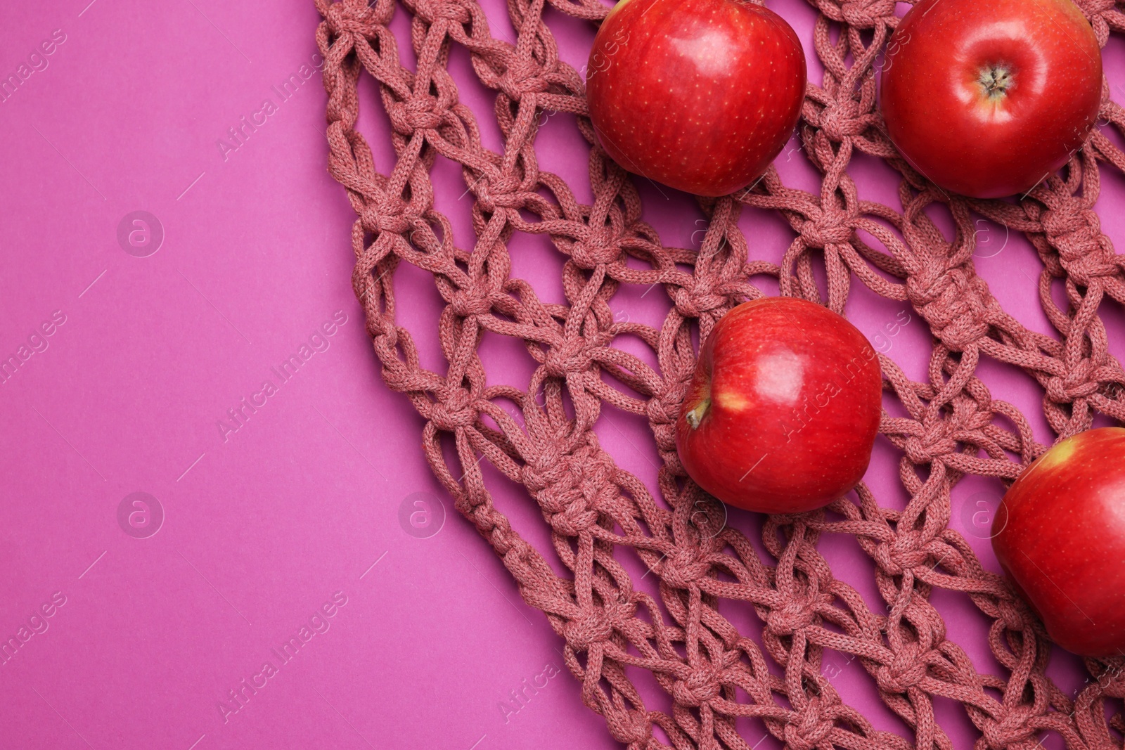 Photo of Handmade macrame shopping bag with apples on crimson background, top view