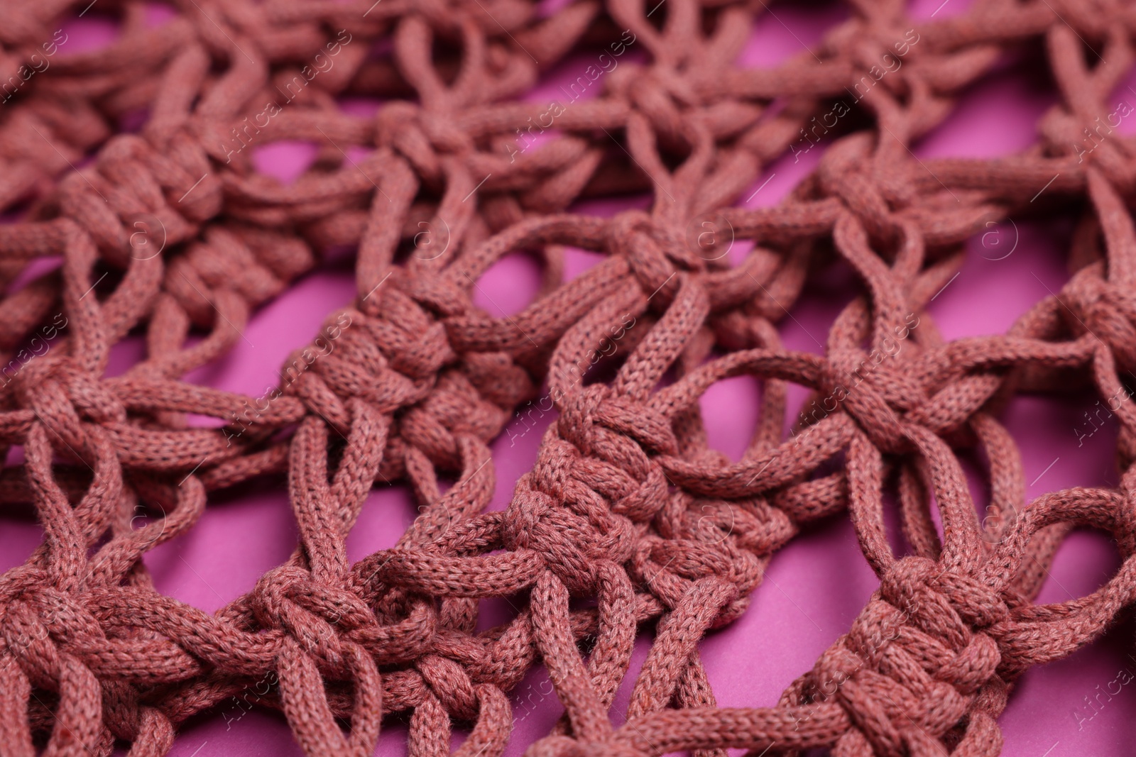 Photo of Handmade macrame shopping bag on crimson background, closeup