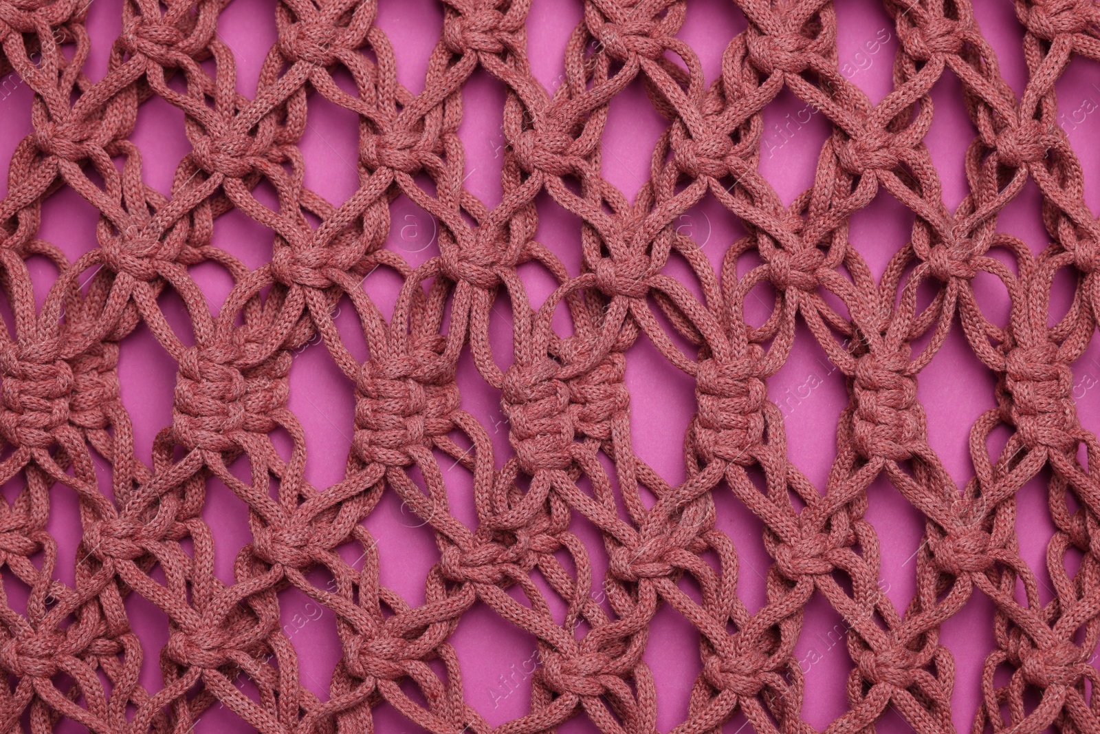 Photo of Handmade macrame shopping bag on crimson background, closeup