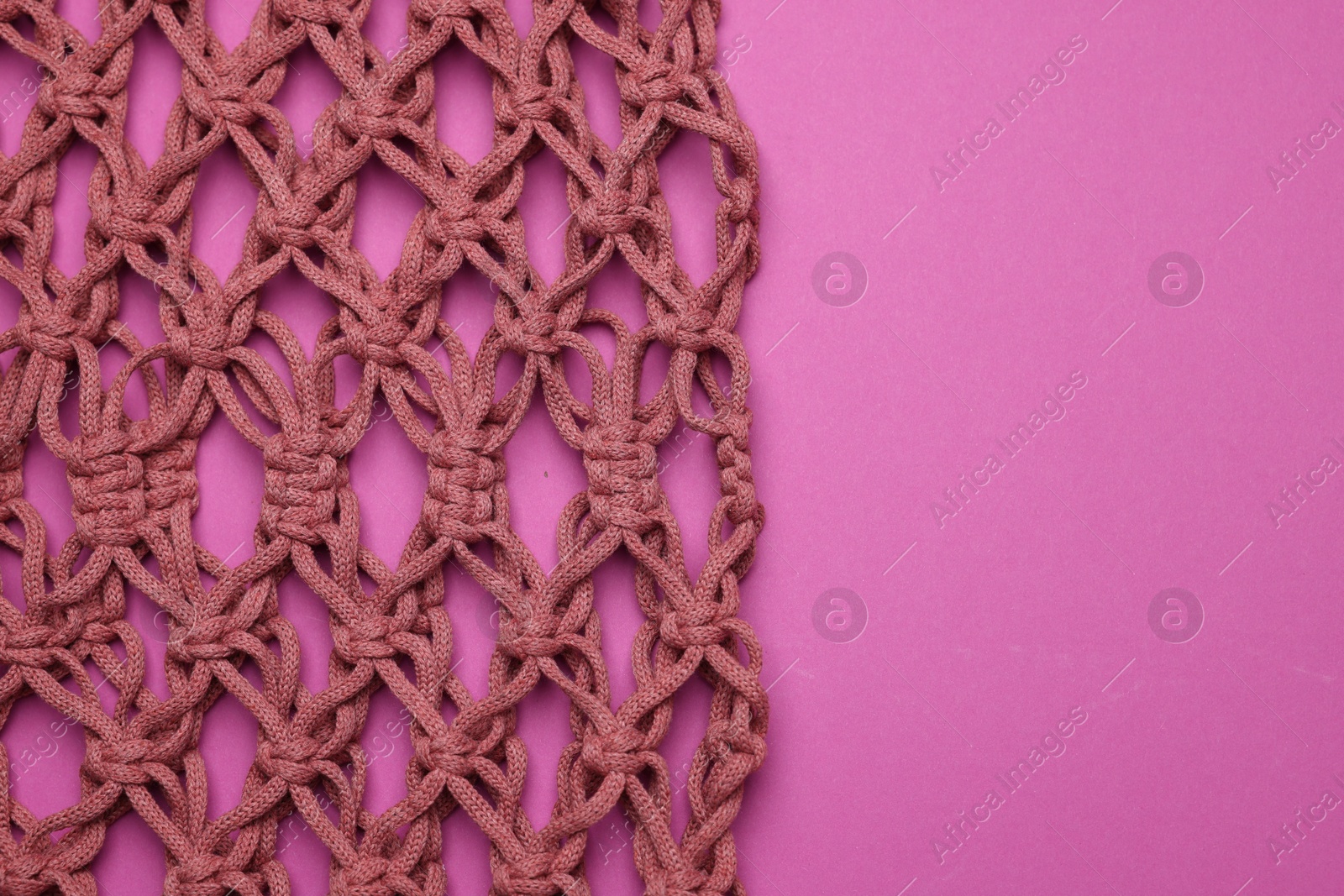 Photo of Handmade macrame shopping bag on crimson background, top view. Space for text