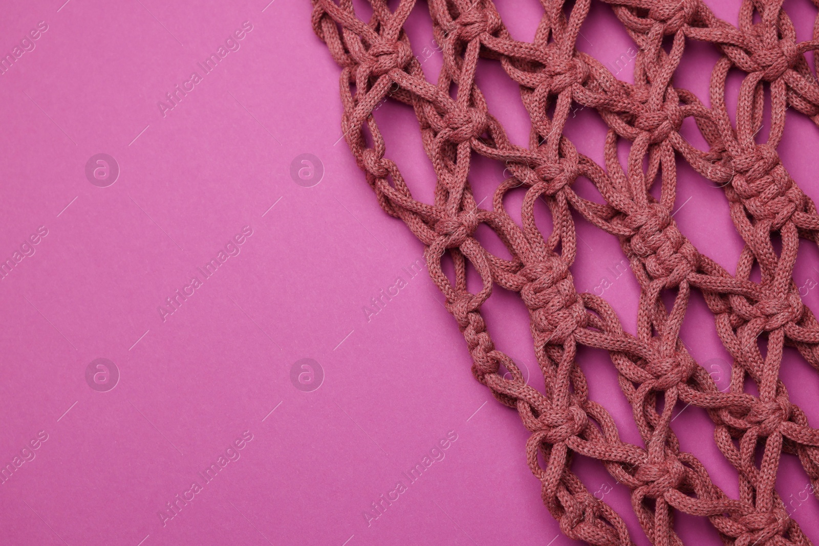 Photo of Handmade macrame shopping bag on crimson background, top view. Space for text